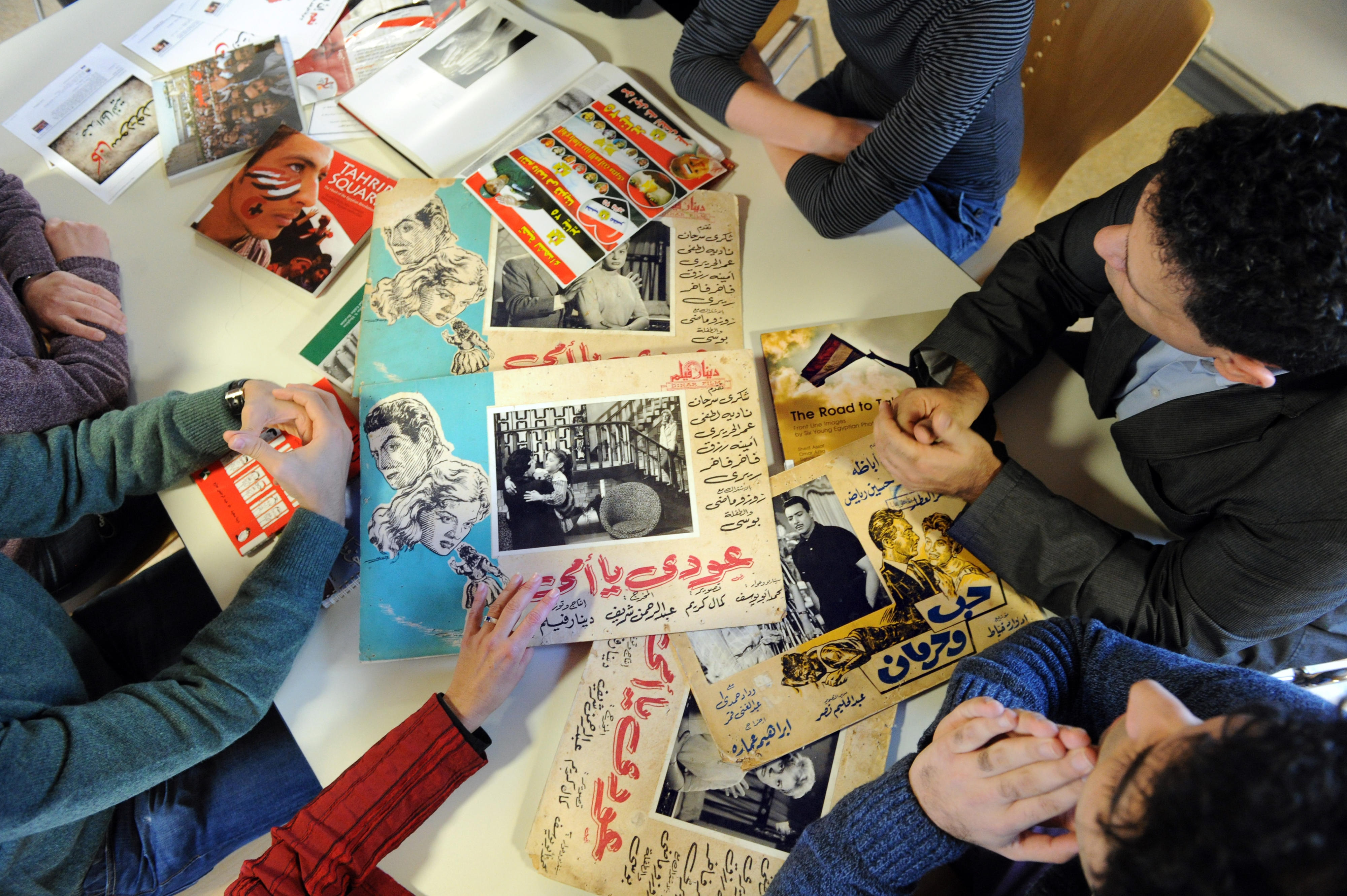 A desk full with printouts, hands of people 