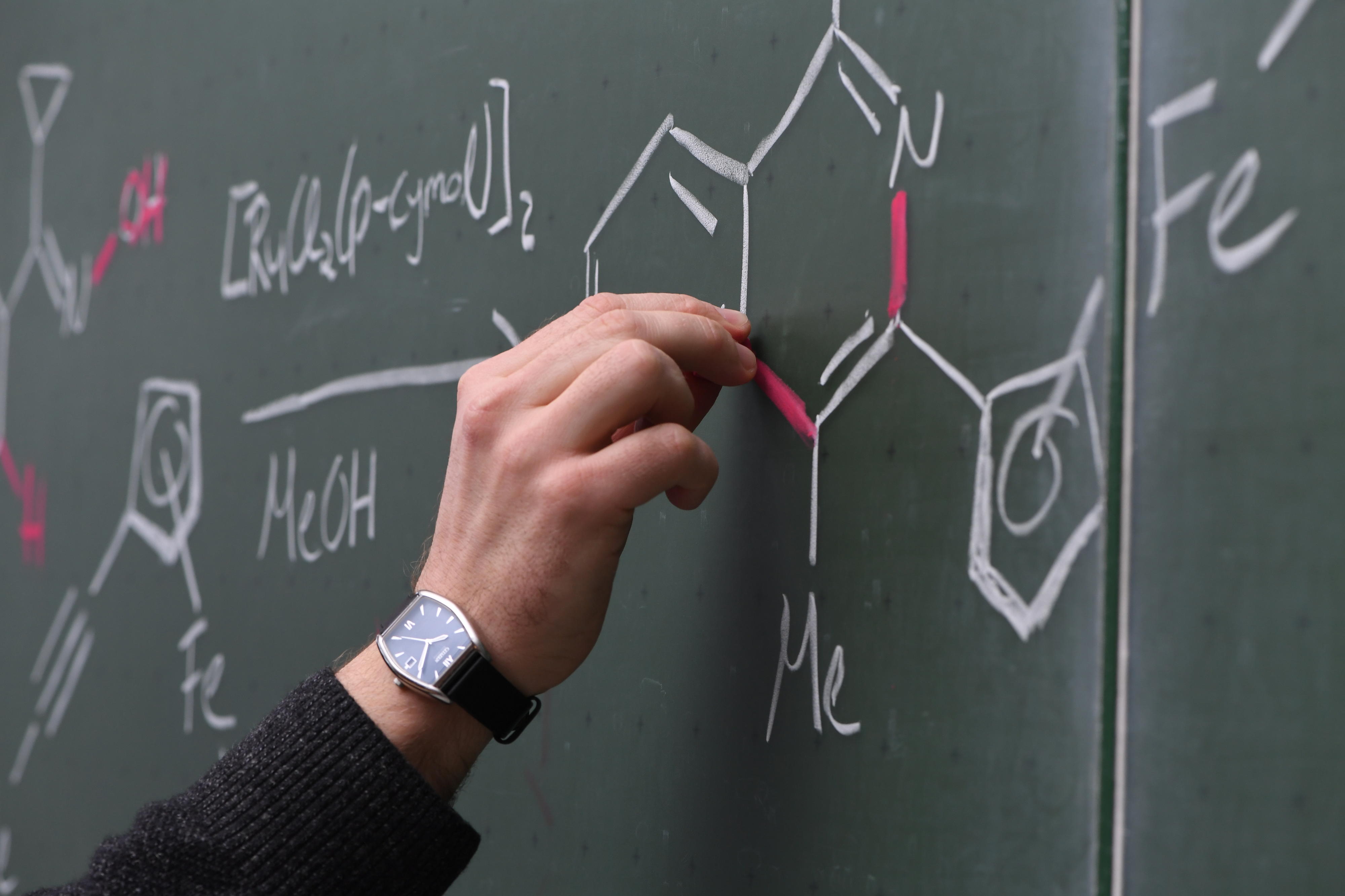 A hand writing formulas on a whiteboard